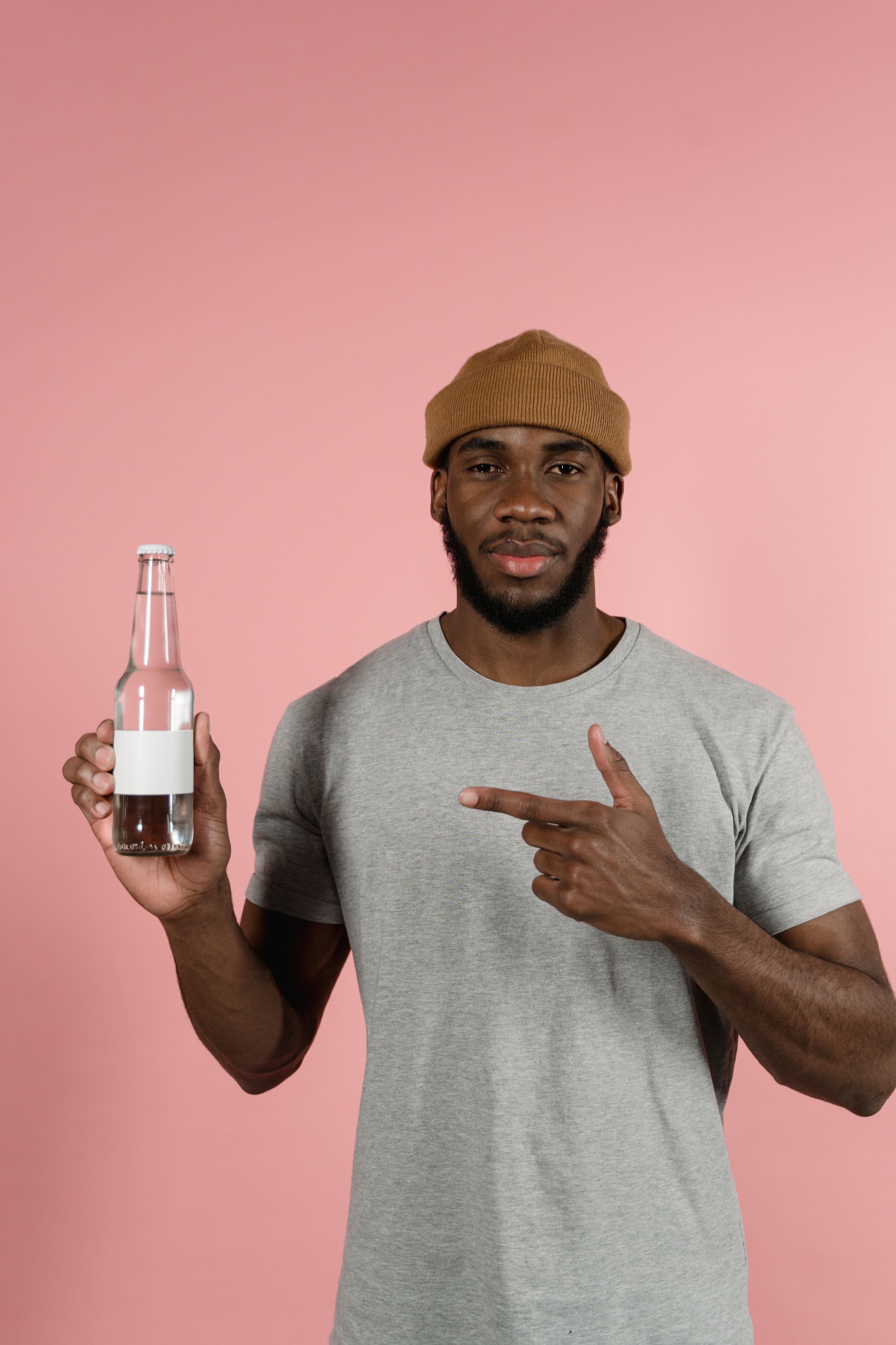 Black man in a studio holding and pointing at a glass bottle against a pink backdrop.
