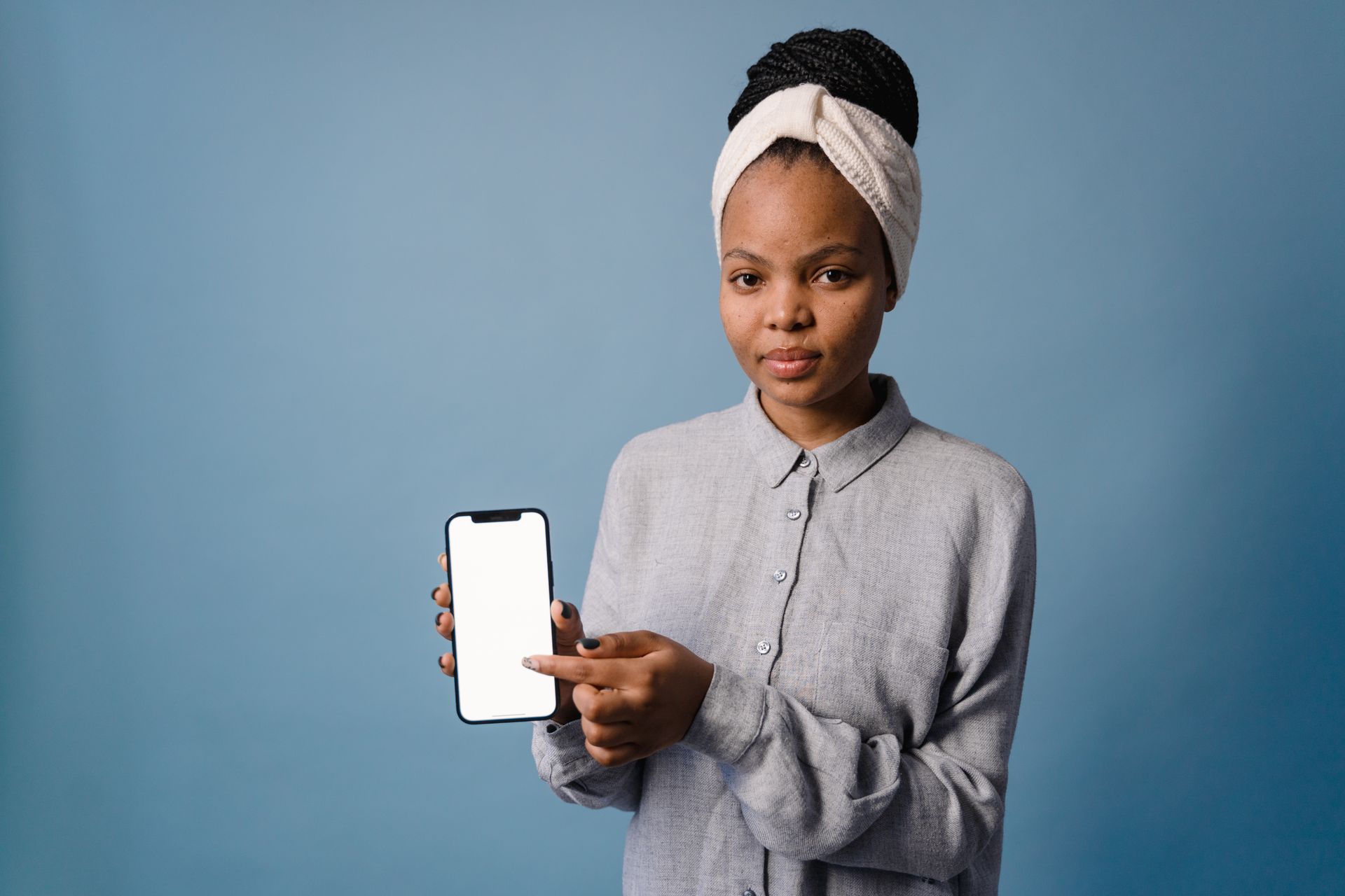 Confident woman displaying smartphone with blank screen against a blue backdrop.