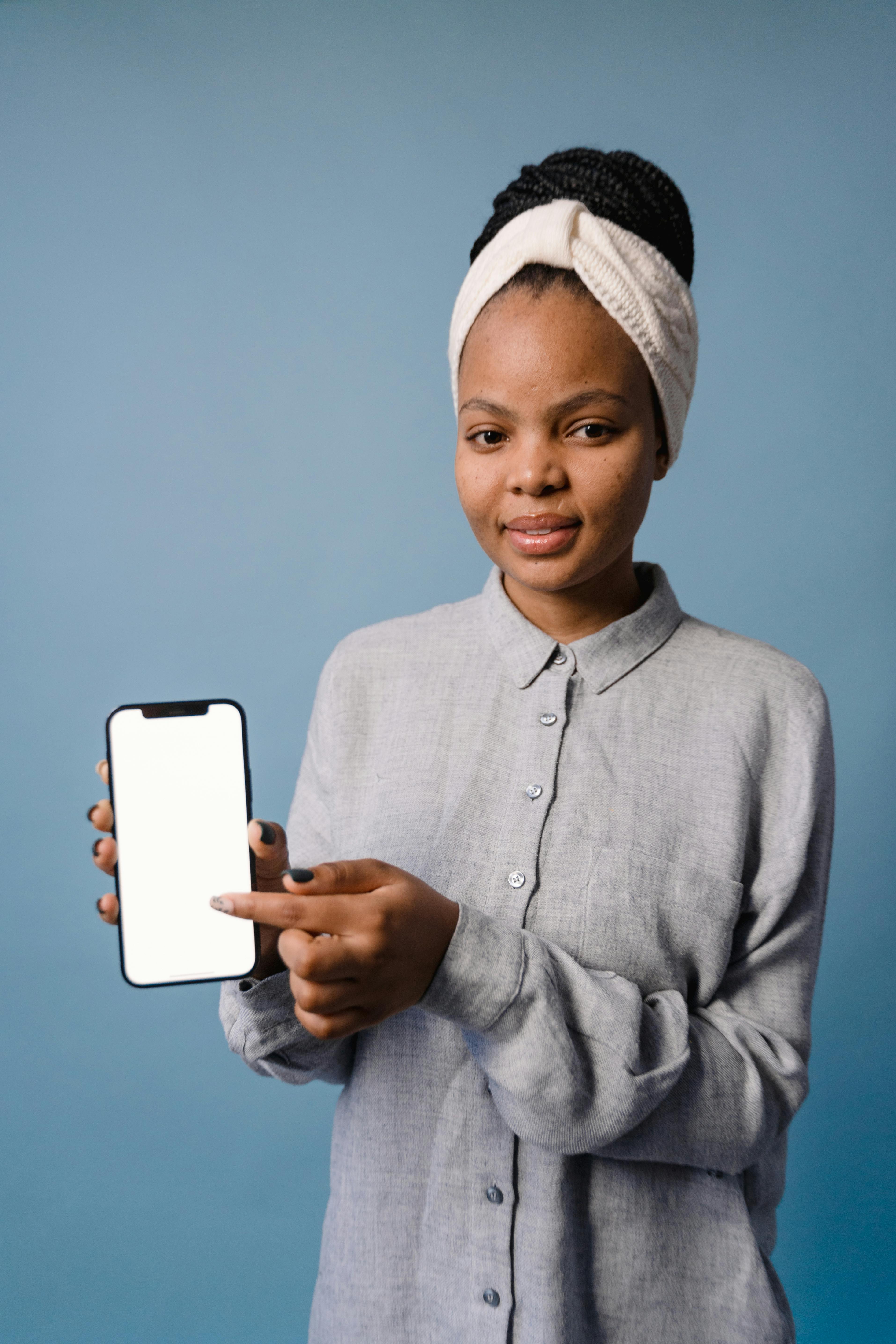 Portrait of a woman in gray attire displaying a smartphone with a blank screen on a blue backdrop.
