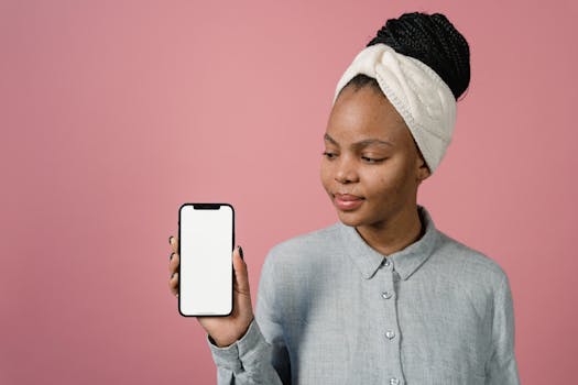 Young black woman displaying a mobile phone screen on a pastel pink backdrop.