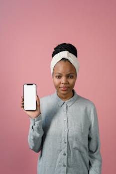 Portrait of a woman with smartphone against pink backdrop in studio setting.
