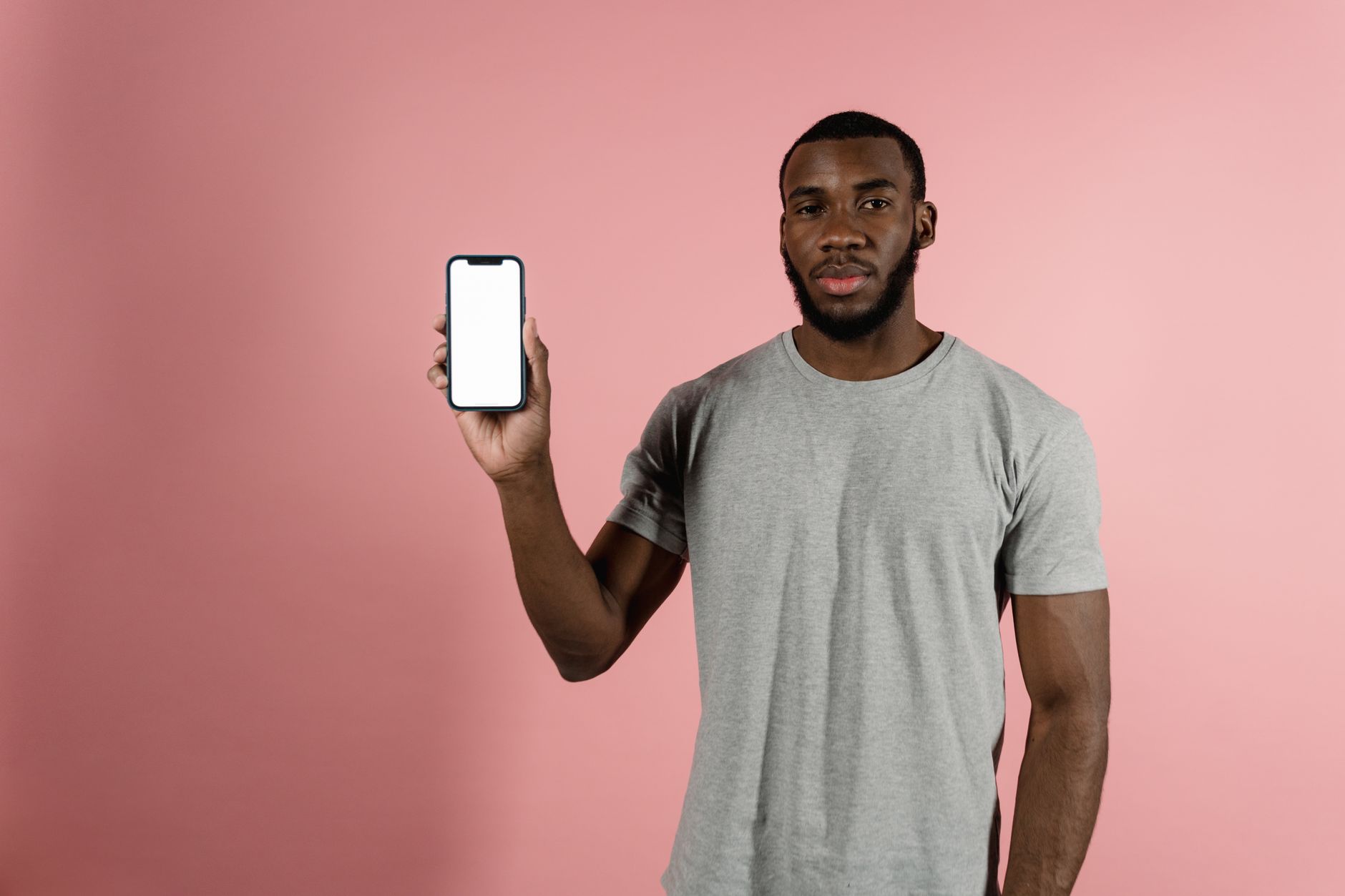 Man in gray shirt holding a smartphone with a blank screen against a pink background.