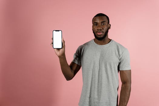 Man in gray shirt holding a smartphone with a blank screen against a pink background.