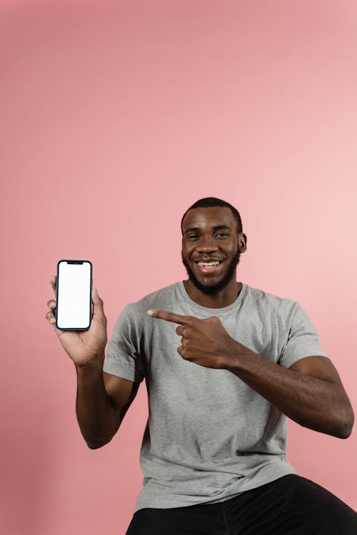 Free Man in Gray Shirt Smiling while Pointing at the Smartphone  Stock Photo