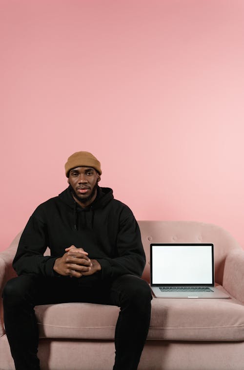 Man in Black Sweater Sitting on Brown Sofa beside Laptop