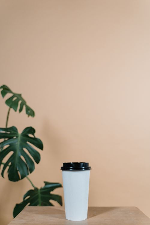 Free A white coffee cup with black lid on a wooden table against a beige background. Stock Photo