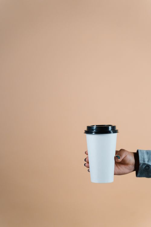 Free A minimalist coffee cup held by a woman's hand against a beige background, offering ample copyspace. Stock Photo