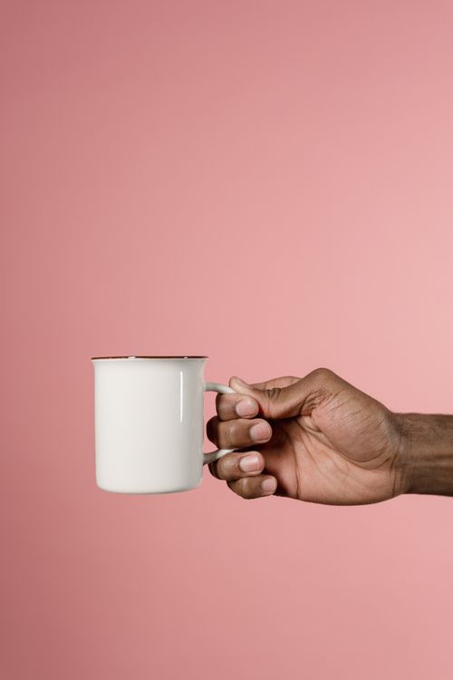 Free Close-up of an adult hand holding a white mug against a solid pink background. Stock Photo