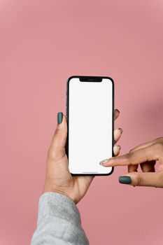 Close-up of hands holding a smartphone with a blank screen against a pink background.