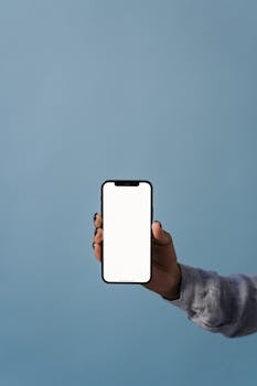 A hand holds a blank-screen smartphone against a blue background, perfect for mockups.