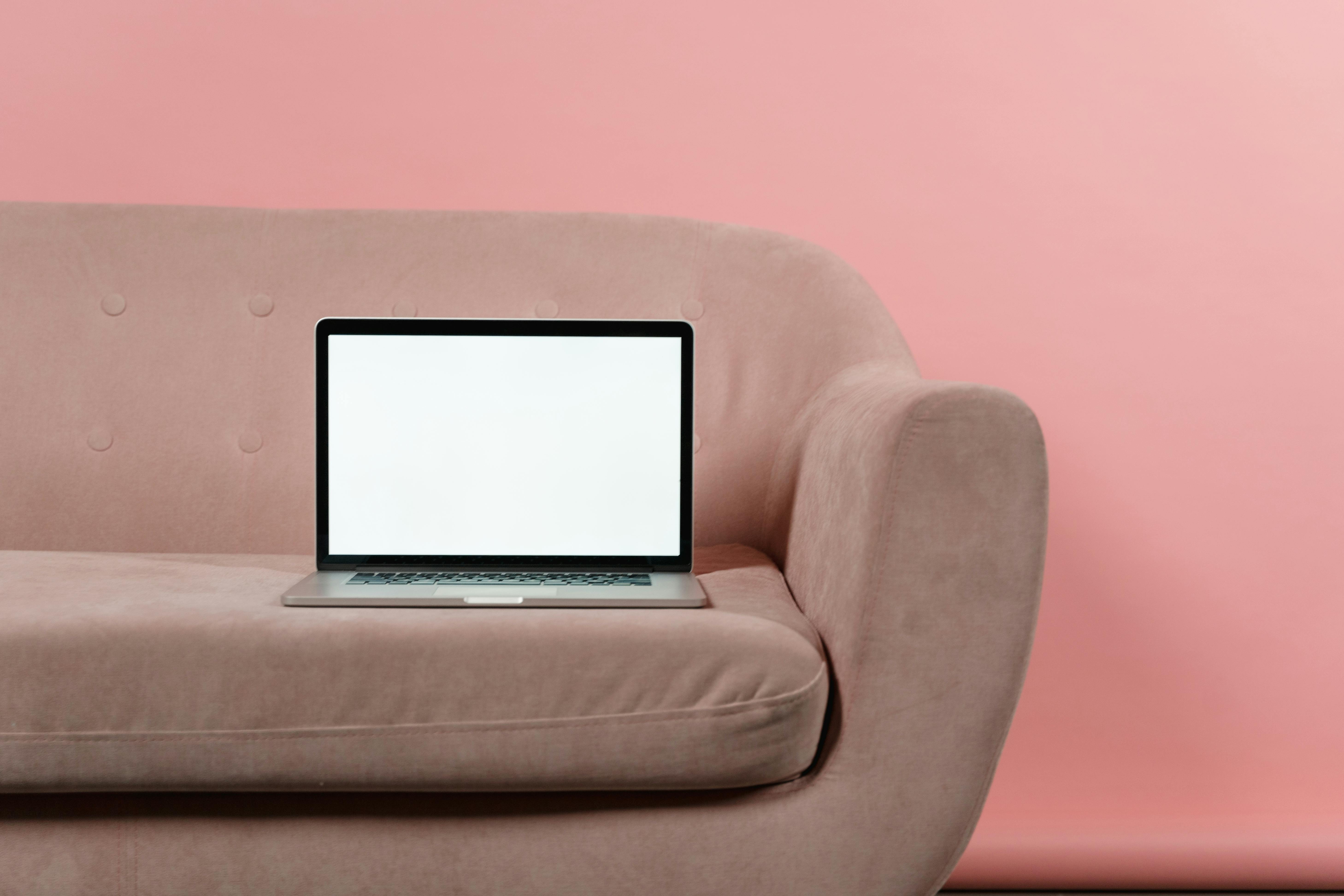 A minimalist laptop mockup displayed on a light pink sofa against a pink background, perfect for digital presentations.