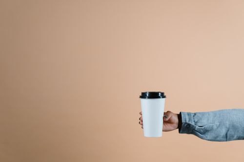 Free A simple photo of a hand holding a coffee cup against a beige background with copyspace. Stock Photo