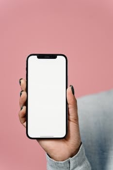 Close-up of a hand holding a smartphone with a blank screen against a pink background.