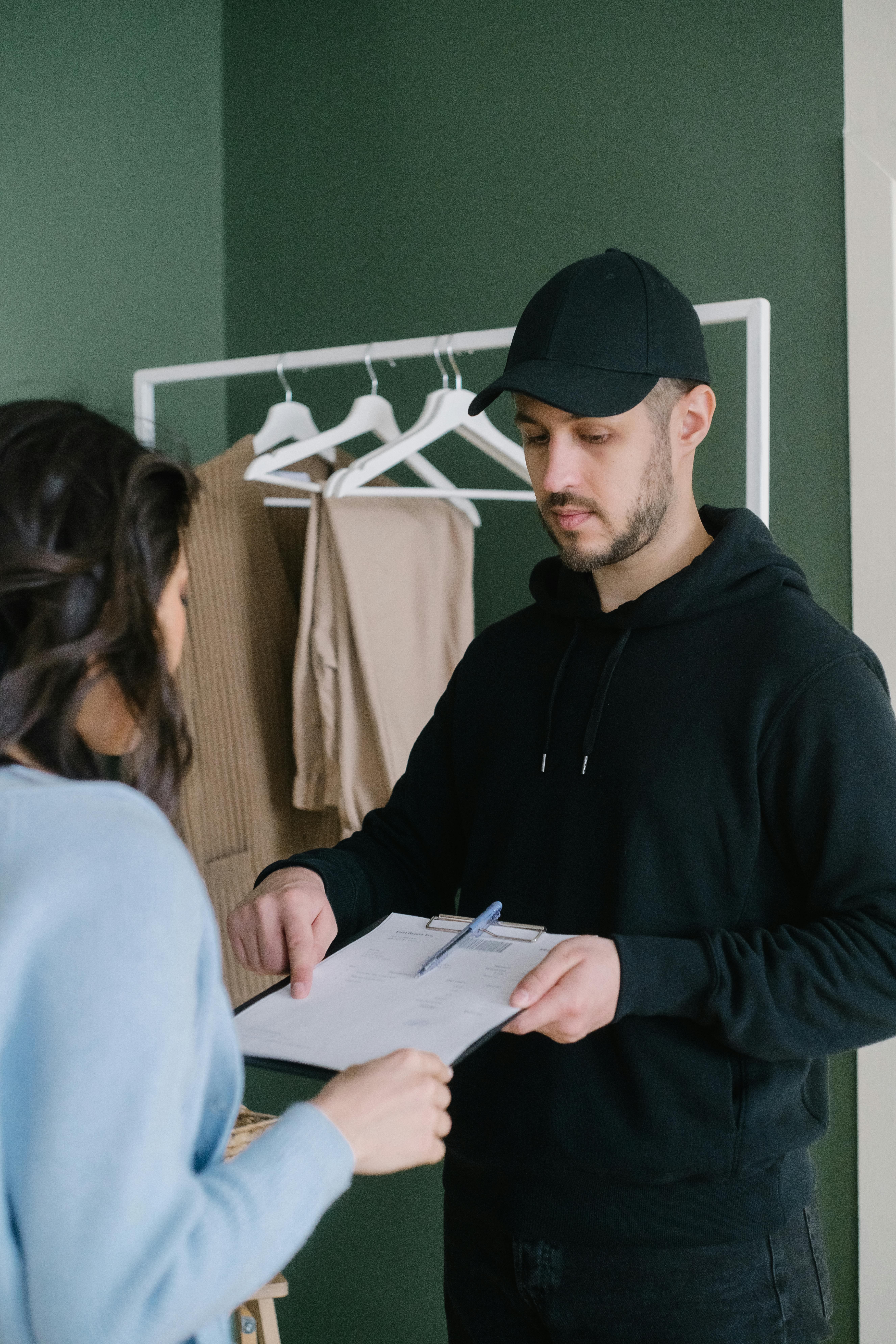 Delivery person handing over clipboard to woman in home setting with clothes in background.