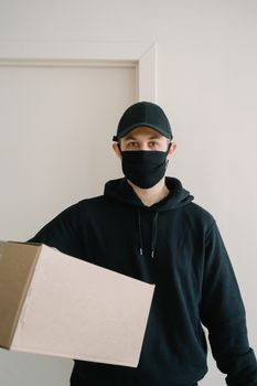 A masked courier in a black hoodie delivers a package with a professional demeanor.