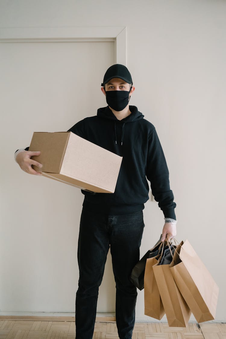 A Man In Black Hoodie Carrying A Box And Shopping Bags