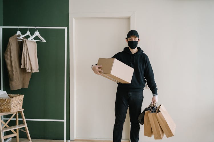 A Man In Black Hoodie Carrying A Box And Shopping Bags