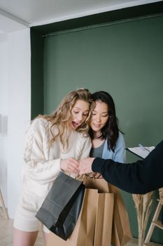Two women joyfully receive shopping bags from a delivery courier indoors, showcasing surprise and happiness.