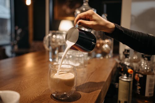 A Person Pouring Milk on a Glass of Coffee