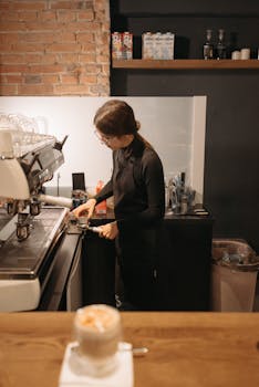 A barista preparing coffee using an espresso machine in a warm, inviting cafe setting.