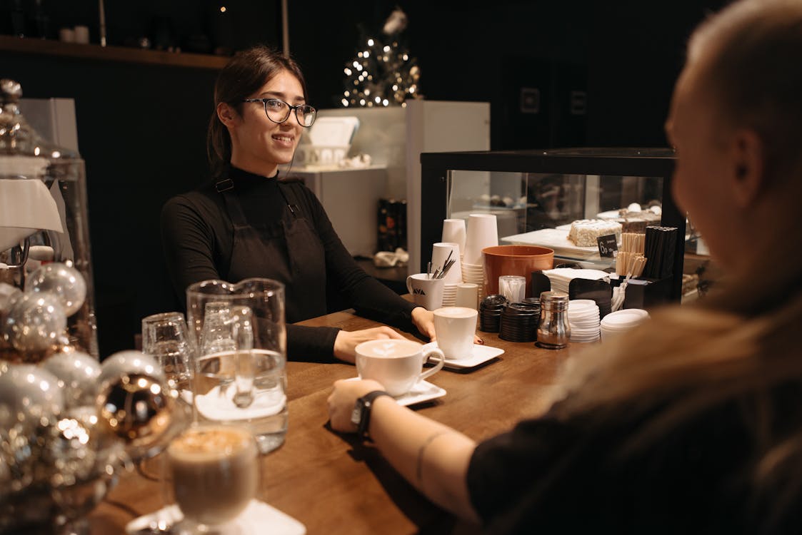 Free A Woman in Black long Sleeves and Apron Serving Coffee Stock Photo