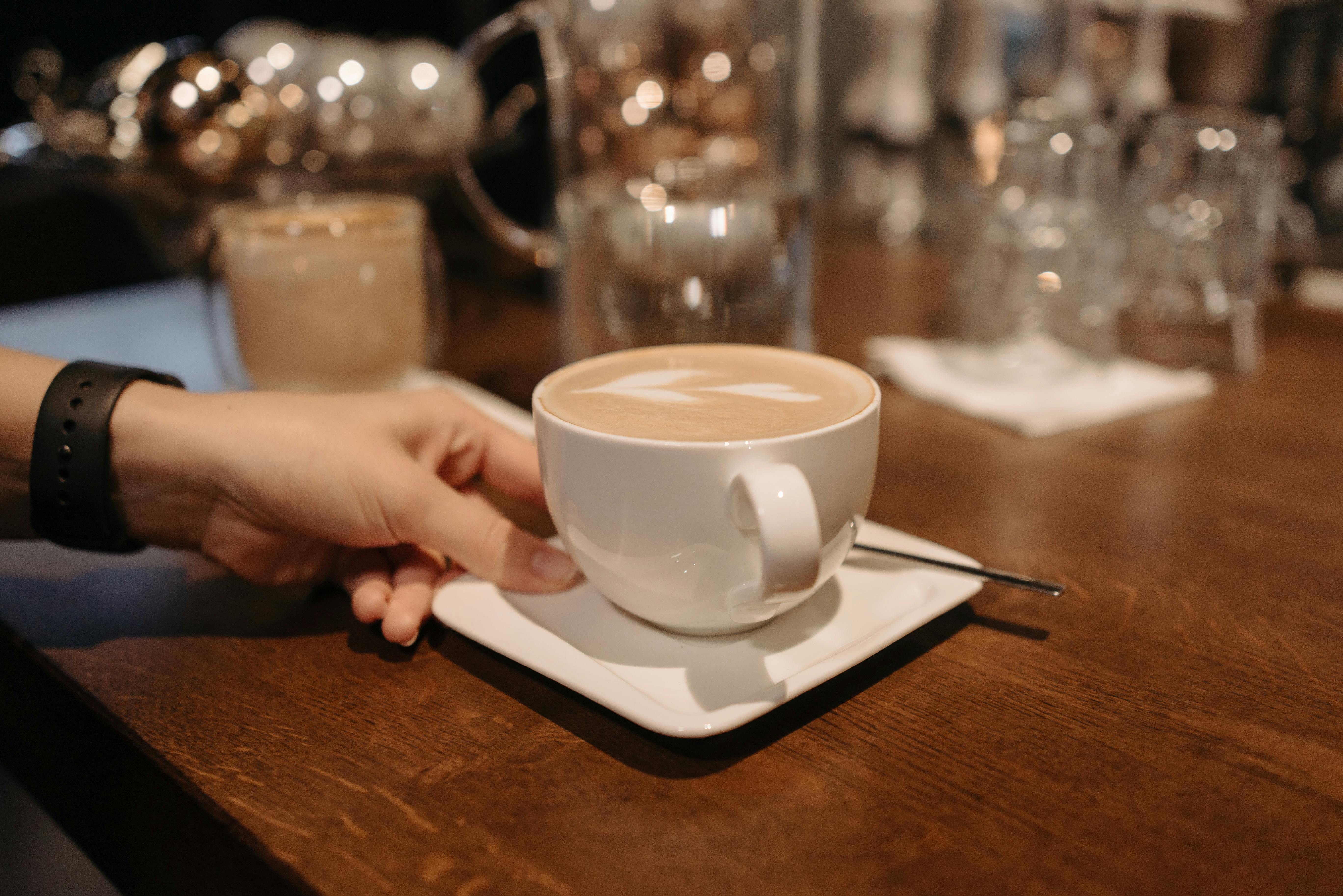 A close-up of a latte with foam art in a cup, resting on a saucer on a wooden table.
