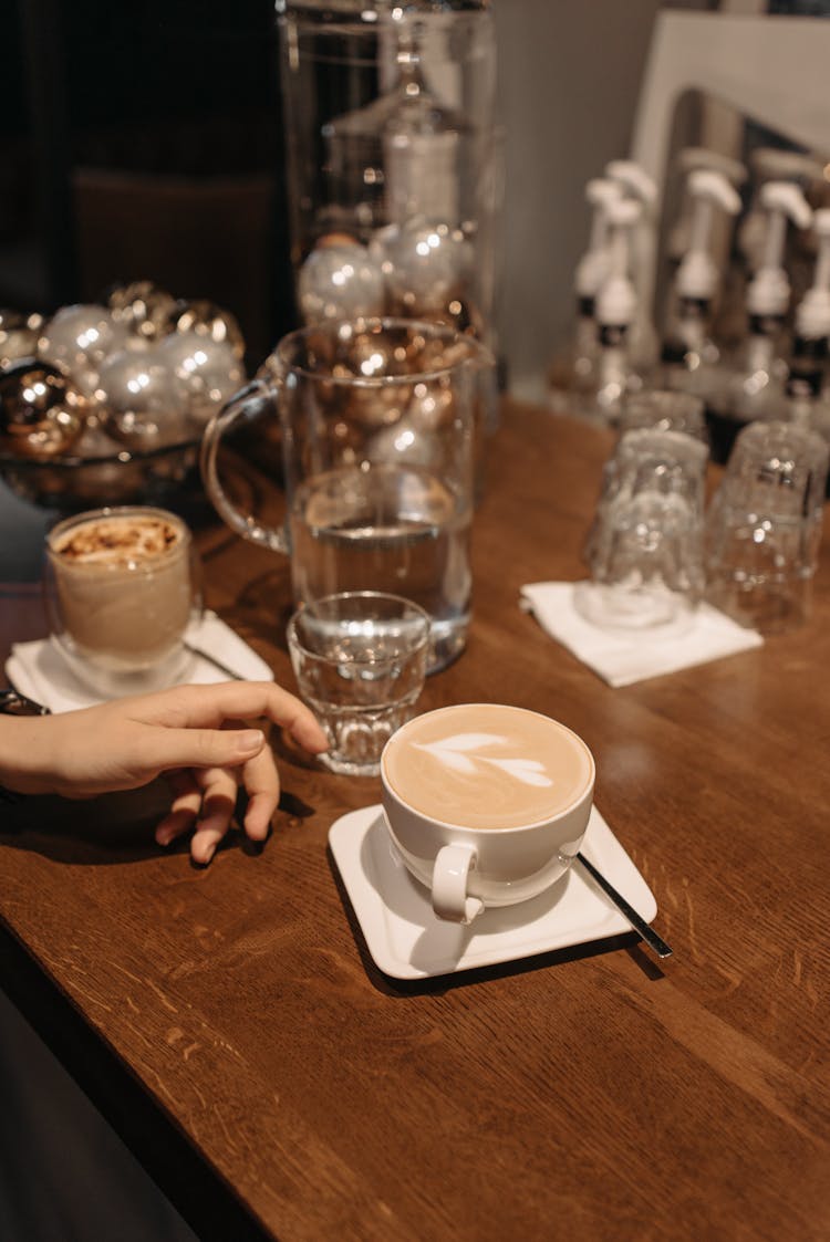 A Hand About To Get The Cup Of Coffee On The Wooden Table