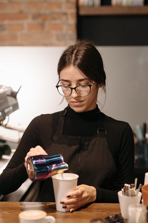 A Female Barista in Black Apron Making a Coffee Drink