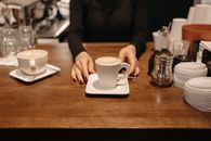 Person Holding White Ceramic Mug on Brown Wooden Table