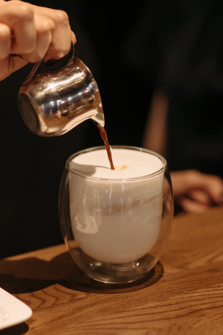 A Hand Pouring Coffee On A Glass With Milk