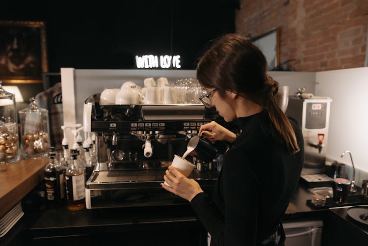 A Woman Pouring Milk On A Cup Of Coffee