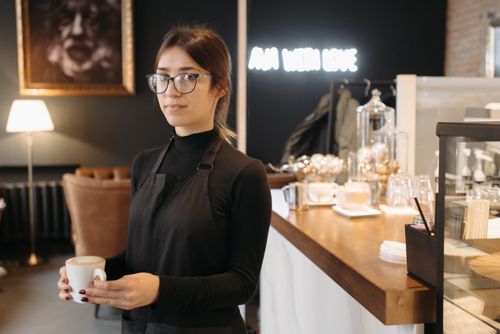 Free A barista holding a cup of coffee in a cozy café with warm lighting and stylish decor. Stock Photo