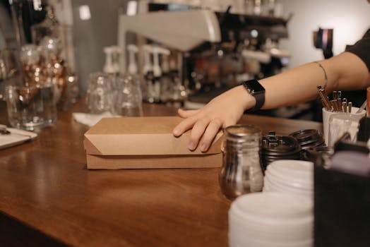 Barista handing over a takeout box at a café counter. Ideal for business and service imagery.