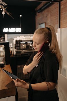 Female barista multitasking with phone and tablet in cozy coffee shop setting.