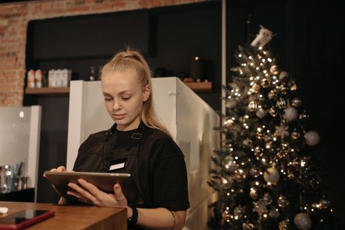 Free A barista works on a tablet in a cozy café with Christmas decorations. Stock Photo