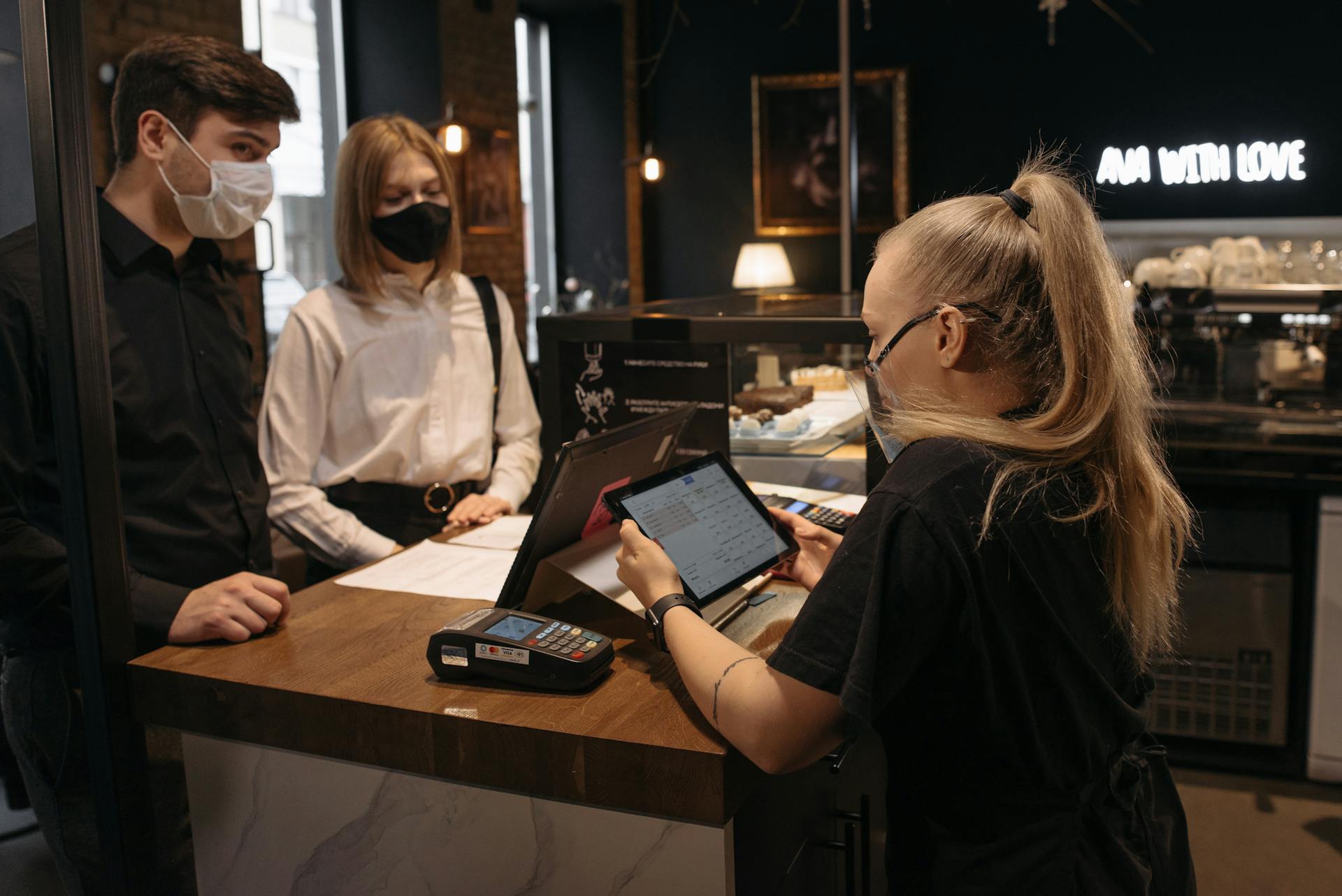 Customers place an order at a café counter with a barista using a tablet for payment.