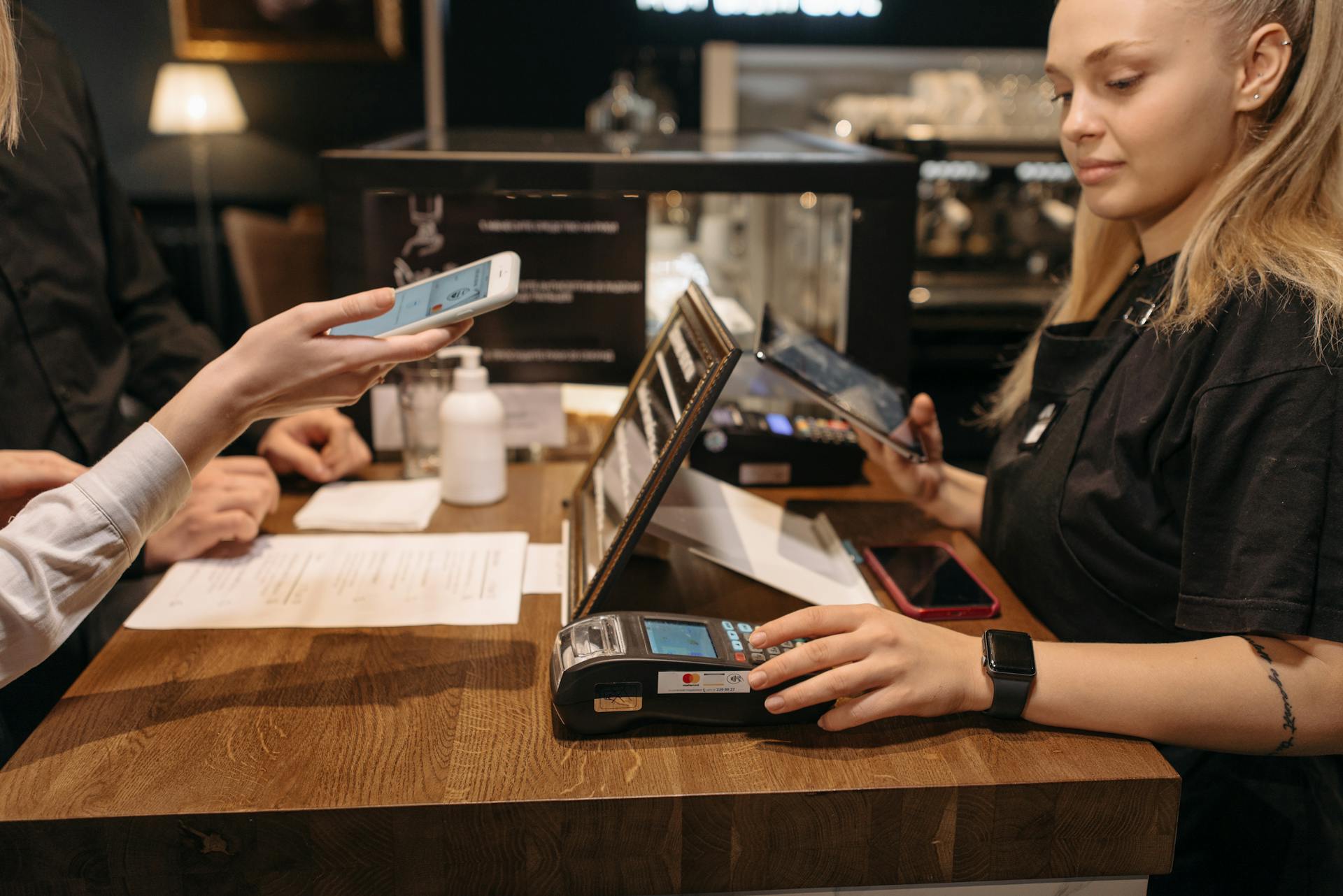 A Woman in Black Shirt Using a Payment Terminal at the Counter