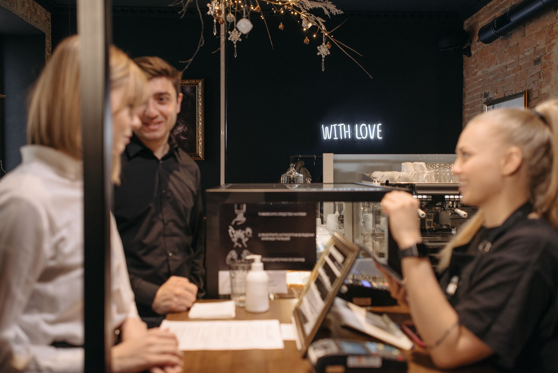 Customers engaging with a barista in a cozy coffee shop featuring warm lighting and decor.