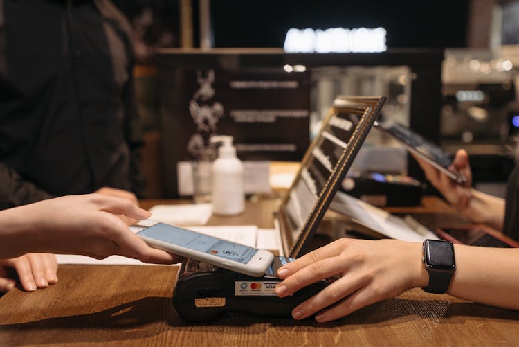 A Person Tapping The Phone On A Payment Terminal