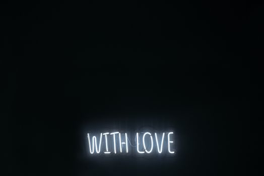 A minimalist neon sign glowing 'With Love' on a dark background, creating a warm ambiance.