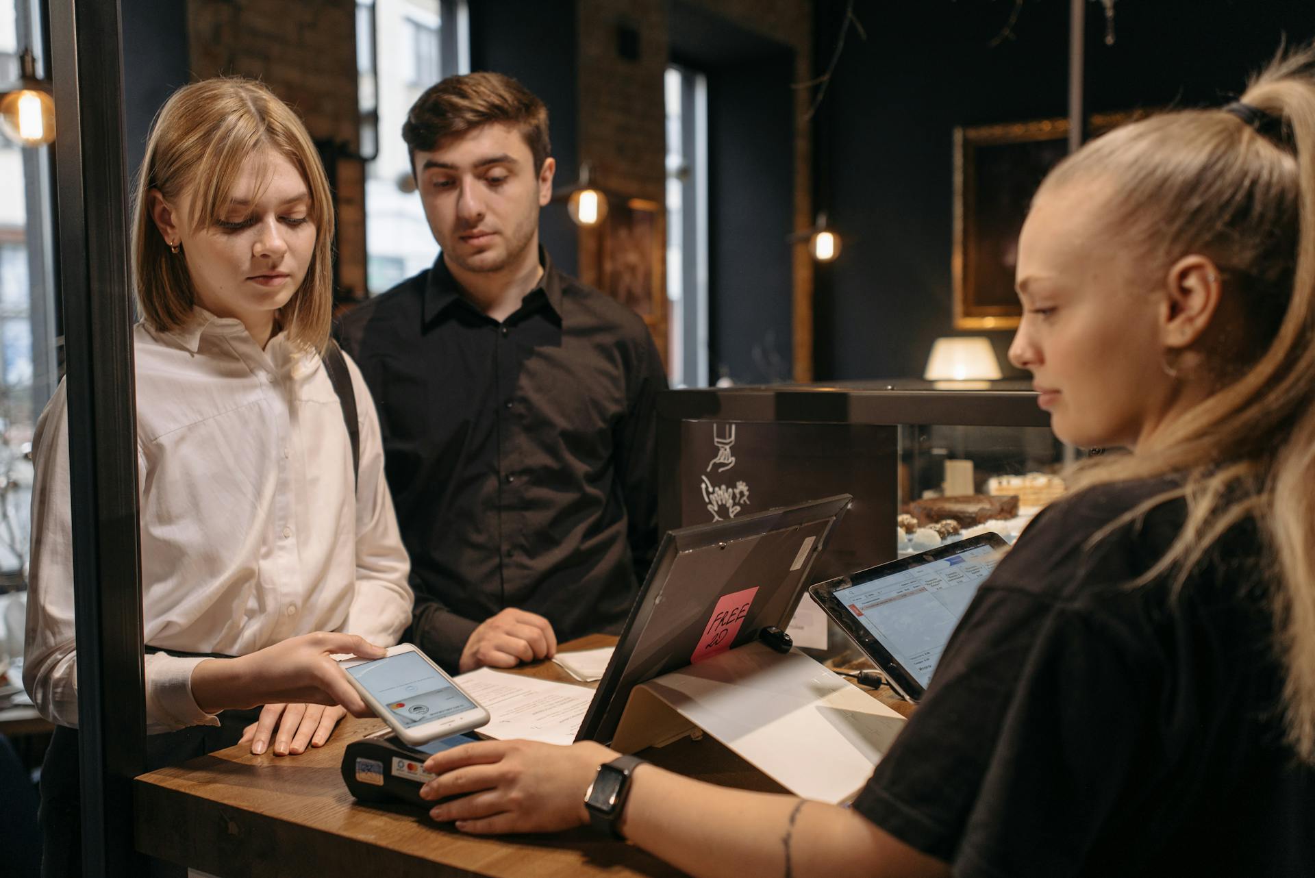 A Woman in White Long Sleeves Tapping Her Phone on a Payment Terminal at the Counter