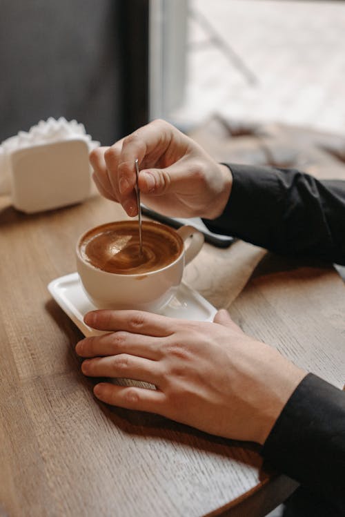 Person Stirring Coffee in a Ceramic Cup