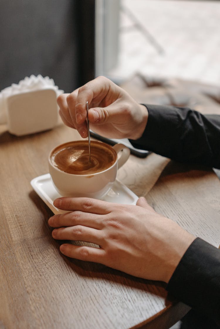 Person Stirring Coffee In A Ceramic Cup