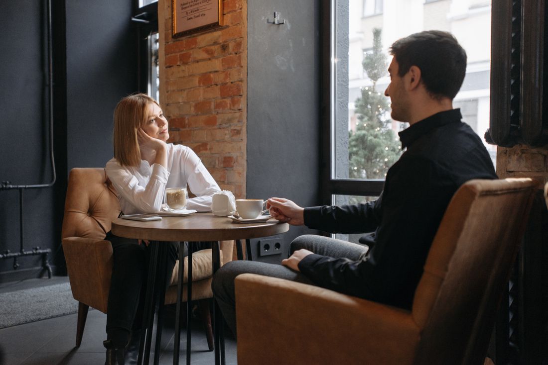 Two people in conversation over coffee by a window in a dim cafe — photo by Pavel Danilyuk on Pexels