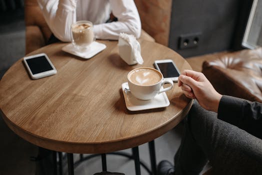 Two people enjoying coffee at a round wooden table indoors with smartphones.