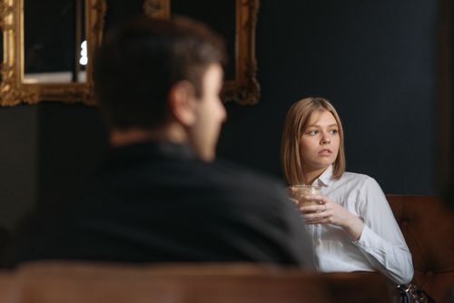 Free A woman sits thoughtfully in a cafe holding a drink, looking away with an introspective expression. Stock Photo