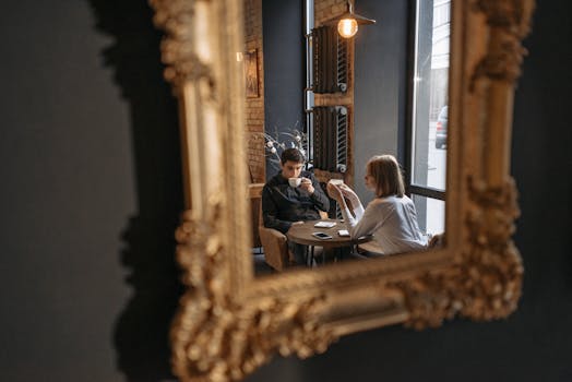 A couple enjoying coffee, seen through a decorative mirror in a cozy café setting.