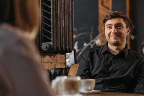 Free Young man in a black shirt enjoying a conversation in a cozy cafe. Stock Photo