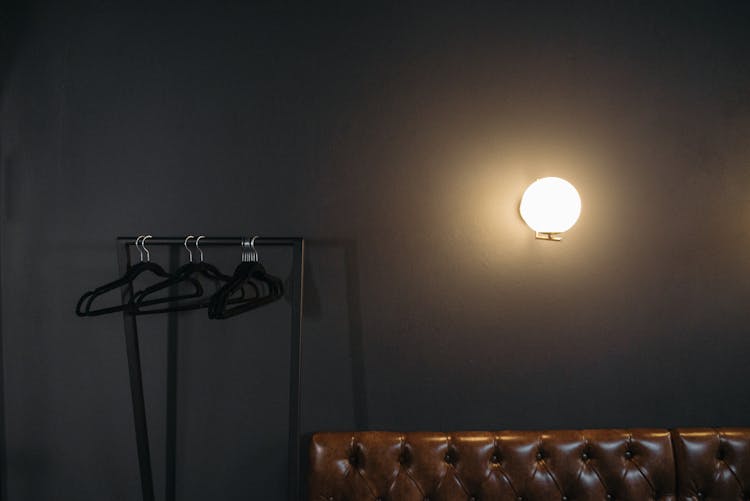 A Light On Gray Wall Near Black Hangers Hanging On Rack