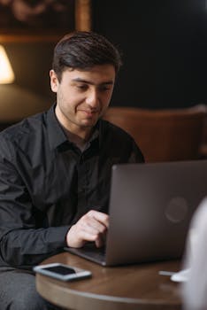 Adult man in black shirt using a laptop indoors, creating a productive ambiance.